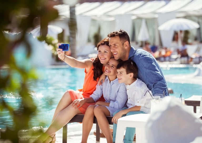 Family of four taking a selfie together by a resort pool on a sunny day