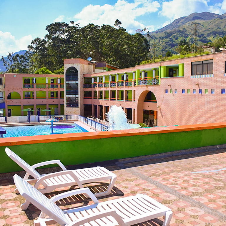 Colorful resort with white lounge chairs overlooking a swimming pool, fountain, and mountain landscape