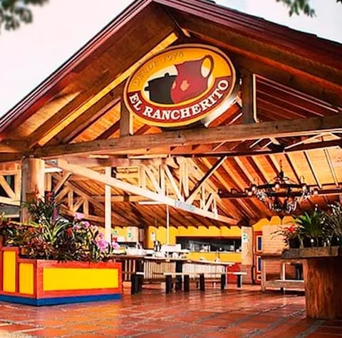 Rustic wooden restaurant exterior with El Ranchero neon sign, wooden beams, and colorful awning