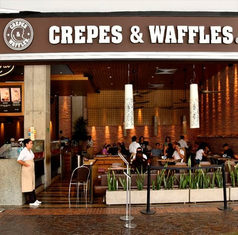 Crepes & Waffles storefront with brown brick interior, diners seated at tables, and white pendant lights overhead