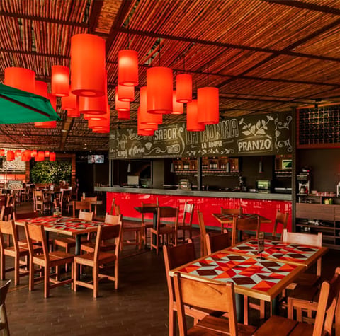 Modern restaurant interior with red hanging lanterns, wooden tables and chairs, red bar seating, and black menu boards above the counter