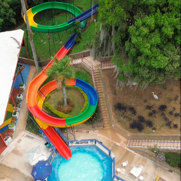 Aerial view of colorful water slides at a theme park with multiple spiral and curved slides in red, orange, green, and blue, leading to a turquoise pool below
