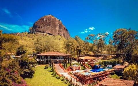 Large granite dome mountain overlooking a sprawling recreational facility with red-roofed buildings, manicured grounds, and scattered trees under blue sky