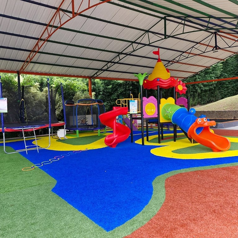 Colorful outdoor playground with multiple slides, climbing structures, and rainbow-colored castle tower covered by metal roof canopy